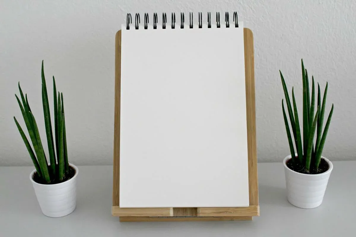 A blank spiral notepad on a wooden stand between two small potted plants