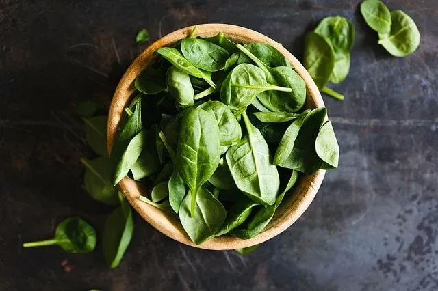 Fresh green leaves in a wooden bowl on a dark surface