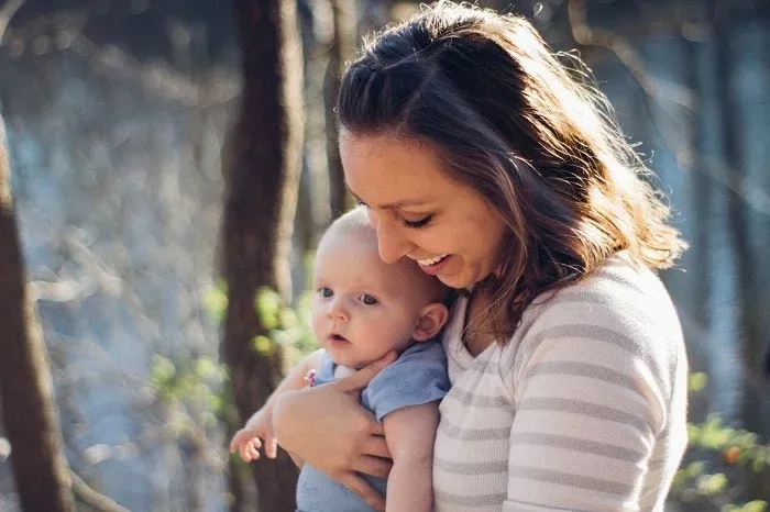 Smiling woman holding a baby outdoors among trees