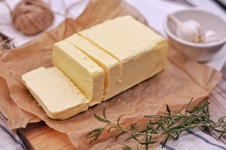 Block of butter cut into slices on baking paper next to a rosemary sprig