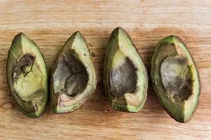 Quatre moitiés d’avocat brunies, noyau retiré, sur une planche en bois