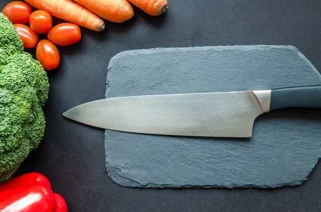 A chef's knife on a slate board, ringed by vegetables