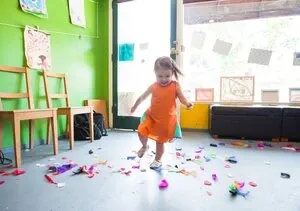 Petite fille en robe orange dansant dans une salle couverte de confettis