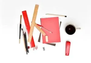 Règles, crayons, cahier rouge, agrafeuse et tasse de café sur fond blanc