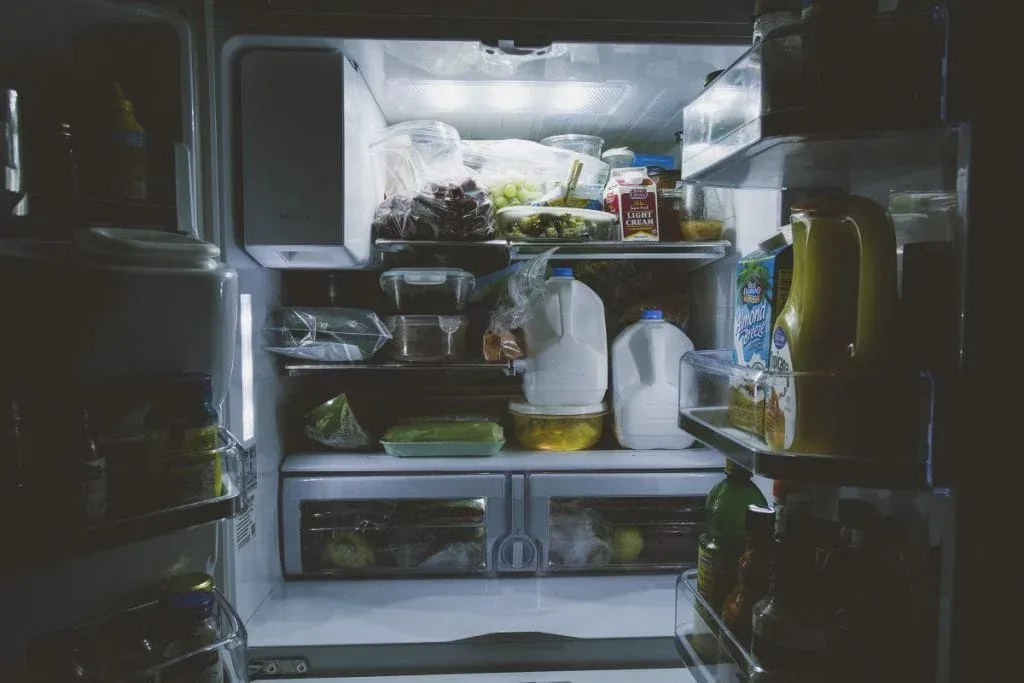 Open refrigerator with milk jugs, containers and bottles on the shelves
