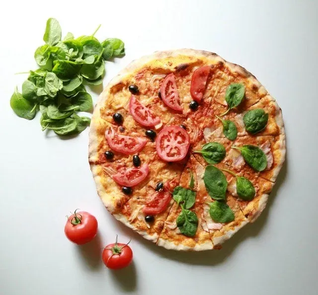 Pizza aux tomates, olives noires et épinards avec des tomates entières