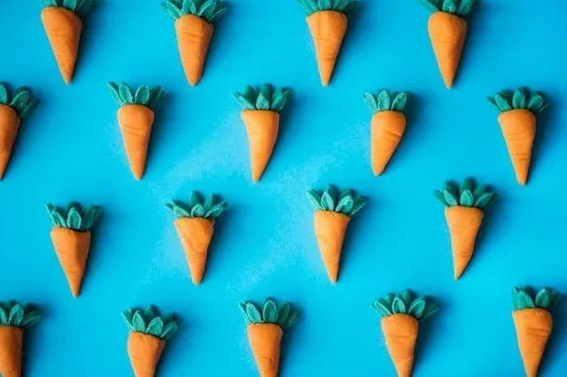 Petites carottes en pâte orange à feuilles vertes sur fond bleu