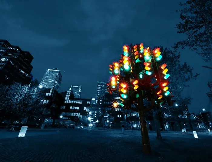 Sculpture d’arbre de feux tricolores allumés, de nuit, entre des immeubles