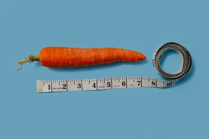 Carotte posée à côté d’un mètre ruban déroulé sur fond bleu